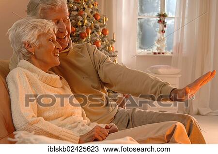 Stock Image - Mature couple in love sitting on a sofa in front of a Christmas tree. Fotosearch