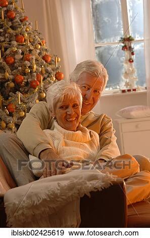 Mature couple in love sitting on a sofa in front of a Christmas tree View Large Photo Image Stock Photo - Mature couple in love sitting on a sofa in front of a Christmas tree. Fotosearch