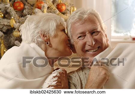 Stock Image - Mature couple in love wrapped in a blanket sitting in front of a Christmas tree. Fotosearch