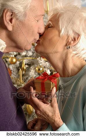 Stock Photograph - Mature couple kissing and exchanging presents in front of a Christmas tree. Fotosearch