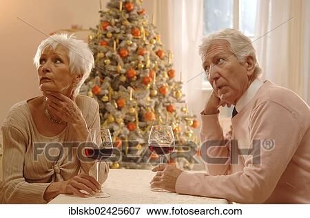 "Mature couple sitting at a table with glasses of red wine, looking annoyed, in front of a Christmas tree" View Large Photo Image Stock Photo - "Mature couple sitting at a table with glasses of red wine, looking annoyed, in front of a Christmas tree". Fotosearch