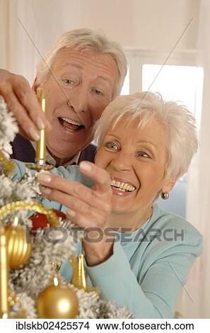 Mature couple smiling while decorating a Christmas tree View Large Photo Image Picture - Mature couple smiling while decorating a Christmas tree. Fotosearch