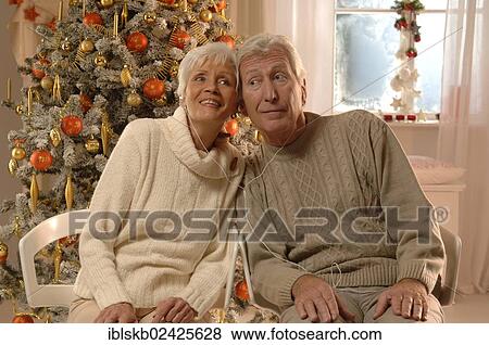 Mature couple with headphones sitting in front of a Christmas tree View Large Photo Image Stock Photo - Mature couple with headphones sitting in front of a Christmas tree. Fotosearch