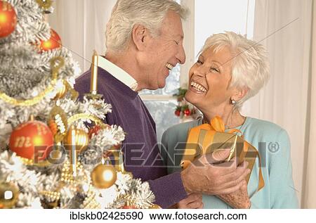 Mature couple with present next to a Christmas tree View Large Photo Image Stock Image - Mature couple with present next to a Christmas tree. Fotosearch