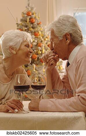 Mature couple with red wine glasses sitting at a table in front of a Christmas tree View Large Photo Image Stock Photography - Mature couple with red wine glasses sitting at a table in front of a Christmas tree. Fotosearch