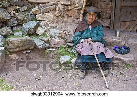 Picture - "Mature Quechua Indian woman wearing a hat sitting on a stone in front of a doorway, Cordillera Huayhuash, Northern Peru, Peru, South America". Fotosearch