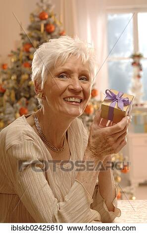 Mature woman holding a gift in front of a Christmas tree View Large Photo Image Stock Image - Mature woman holding a gift in front of a Christmas tree. Fotosearch