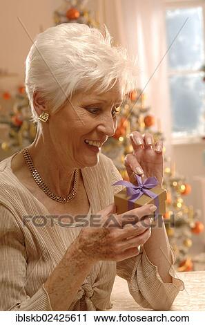Stock Image - Mature woman holding a present in front of a Christmas tree. Fotosearch
