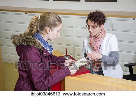 Stock Image - "Medical practice, the receptionist handing over a referral to specialist to a patient, Germany, Europe". Fotosearch