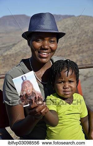 "Modern Himba woman holding her child with a photo of herself wearing traditional dress, Orupembe, Kaokoland, Kunene, Namibia, Africa" View Large Photo Image Stock Photograph - "Modern Himba woman holding her child with a photo of herself wearing traditional dress, Orupembe, Kaokoland, Kunene, Namibia, Africa". Fotosearch