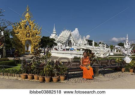 Stock Photo - "Monk sitting in front of the ornate golden entrance of Wat Rong Khun, White Temple, by architect Chalermchai Kositpipat, Chiang Rai, Chiang Rai Province, Northern Thailand, Thailand, Asia". Fotosearch