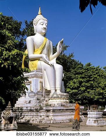 Stock Photo - "Monk standing in front of a white seated Buddha statue at Wat Mahathat, Sukhothai Historical Park, Sukhothai, Sukhothai Province, Northern Thailand, Thailand, Asia". Fotosearch