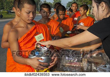 "Morning alms round, a young Buddhist monk from a monastery school holding a begging bowl, receiving food or offerings from a young woman, Sukhothai Province, Northern Thailand, Thailand, Asia" View Large Photo Image Stock Image - "Morning alms round, a young Buddhist monk from a monastery school holding a begging bowl, receiving food or offerings from a young woman, Sukhothai Province, Northern Thailand, Thailand, Asia". Fotosearch