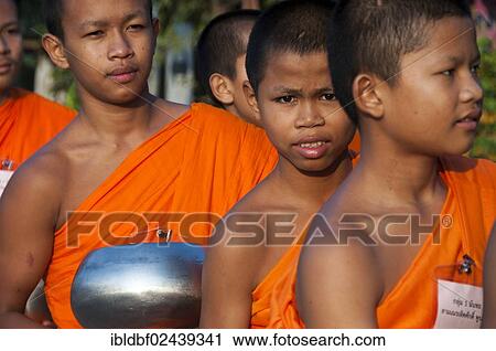 Stock Image - "Morning alms round, young Buddhist monks from a monastery school holding begging bowls, Sukhothai Province, Northern Thailand, Thailand, Asia". Fotosearch