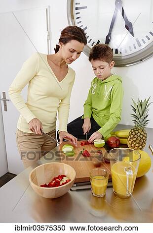 "Mother and son cutting various kinds of fruit on cutting board in a kitchen, Germany, Europe" View Large Photo Image Stock Image - "Mother and son cutting various kinds of fruit on cutting board in a kitchen, Germany, Europe". Fotosearch