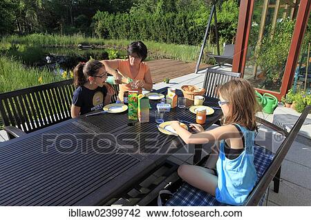 Stock Image - "Mother with two girls, 11, having breakfast on a terrace, Austria, Europe". Fotosearch