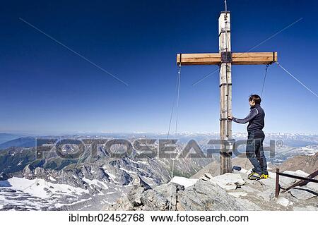 Stock Photo - "Mountain climber at the summit cross of Hochfeiler Mountain, looking over the valleys of Pfitschertal and Wipptal, Alto Adige, Italy, Europe". Fotosearch