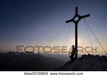 Stock Image - "Mountaineer at the summit cross on Grosser Krottenkopf Mountain at dusk, Allgauer Alpen, Tyrol, Austria, Europe". Fotosearch