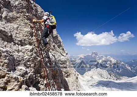 Stock Photo - "Mountaineer climbing the Via Ferrata Ivano Dibona climbing route to the summit of Monte Cristallo to the summit of Cristallino above Cortina, view towards Hohe Gaisl Mountain, Belluno, Dolomites, Italy, Europe". Fotosearch