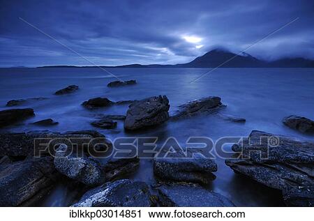 Stock Image - "Mountains shrouded with clouds, blue hour on a rocky seashore, Elgol, Isle of Skye, Scotland, United Kingdom, Europe". Fotosearch
