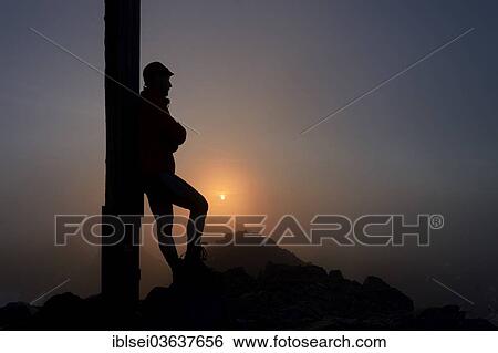 Stock Photograph - "Mt Hohes Licht, mountaineer leaning against the summit cross, Oberstdorf, Oberallgau, Allgau, Swabia, Bavaria, Germany, Europe". Fotosearch