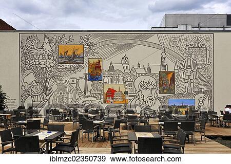 Stock Photo - "Mural paintings depicting Greifswald and a portrait by Caspar David Friedrich, chairs of a cafe in the foreground, Lappstrasse street, Greifswald, Mecklenburg-Western Pomerania, Germany, Europe". Fotosearch