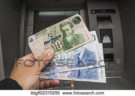 Stock Photography - "Northern Ireland 10 and 20 pound notes held in a hand in front of an ATM, Northern Ireland, United Kingdom, Europe". Fotosearch