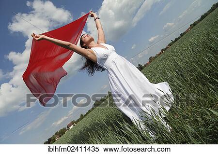 "Oblique view of a young woman wearing a white summer dress in a green corn field while holding a red silk scarf fluttering in the wind, Hagen, Lower Saxony, Germany, Europe" View Large Photo Image Stock Photography - "Oblique view of a young woman wearing a white summer dress in a green corn field while holding a red silk scarf fluttering in the wind, Hagen, Lower Saxony, Germany, Europe". Fotosearch