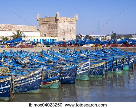 Stock Image - "Old blue fishing boats in the port of Essaouira, behind the fortress of Essaouira, Unesco World Heritage Site, Morocco, Africa". Fotosearch