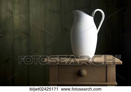Stock Image - Old enamel jug on a small chest of drawers. Fotosearch