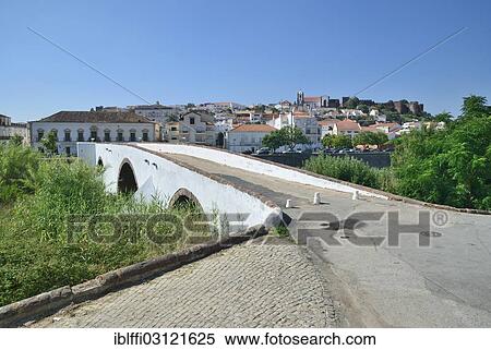 Stock Photography - "Old stone bridge crossing the Rio Arade river, in front of the historic town centre and the medieval castle of Castelo de Silves, Silves, Faro, Algarve, Portugal, Europe". Fotosearch