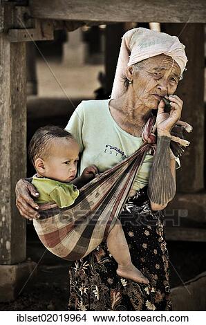 "Old woman, grandmother smoking a cigar, carrying a toddler in a baby sling, in a village on the Mekong River, Laos, Southeast Asia, Asia" View Large Photo Image Picture - "Old woman, grandmother smoking a cigar, carrying a toddler in a baby sling, in a village on the Mekong River, Laos, Southeast Asia, Asia". Fotosearch