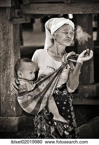 "Old woman, grandmother, smoking a cigar, carrying a toddler in a baby sling, in a village on the Mekong River, Laos, Southeast Asia, Asia" View Large Photo Image Stock Image - "Old woman, grandmother, smoking a cigar, carrying a toddler in a baby sling, in a village on the Mekong River, Laos, Southeast Asia, Asia". Fotosearch