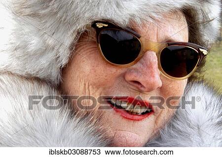 Stock Image - Old woman in a fur coat with a fur hat and sunglasses. Fotosearch