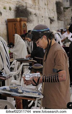 Picture - "Orthodox Jewish boy reading a prayer book with a tefellin on his forehand and phylacteries on his arm, Torah cabinet at back at the Western Wall or Wailing Wall, Muslim Quarter, Jerusalem, Israel, Middle East, Southwest Asia, Asia". Fotosearch