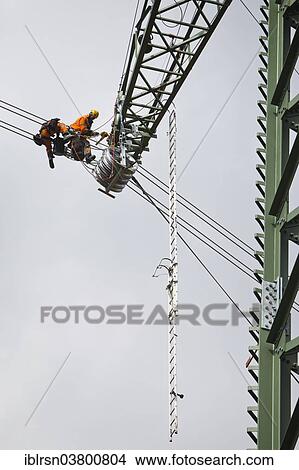 "Overhead transmission cable installers installing insulated cable on the cross arm of a newly built high-voltage transmission mast, Monchenholzhausen, Thuringia, Germany, Europe" View Large Photo Image Picture - "Overhead transmission cable installers installing insulated cable on the cross arm of a newly built high-voltage transmission mast, Monchenholzhausen, Thuringia, Germany, Europe". Fotosearch