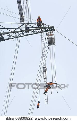 "Overhead transmission cable installers installing insulated cable on the cross arm of a newly built high-voltage transmission mast, Monchenholzhausen, Thuringia, Germany, Europe" View Large Photo Image Stock Image - "Overhead transmission cable installers installing insulated cable on the cross arm of a newly built high-voltage transmission mast, Monchenholzhausen, Thuringia, Germany, Europe". Fotosearch