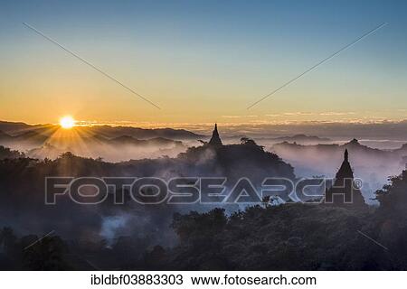 Stock Image - "Pagodas surrounded by trees, at sunrise, in the mist, Mrauk U, Sittwe District, Rakhine State, Myanmar, Asia". Fotosearch