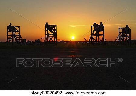 Stock Image - "People sitting on raised seats on Tempelhof Airfield in the evening sun, Berlin-Tempelhof, Tempelhofer Feld, Berlin, Berlin, Germany, Europe". Fotosearch