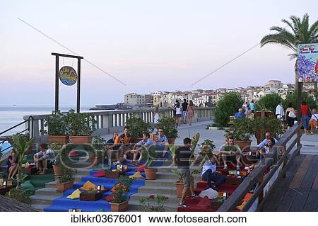 Stock Image - "People sitting on stairs on the promenade, evening mood, Cefalu, Province of Palermo, Sicily, Italy, Europe". Fotosearch