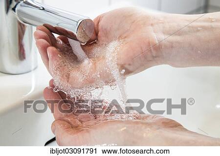 Stock Image - "Person washing their hands under running water from a faucet, symbolic image for water consumption". Fotosearch