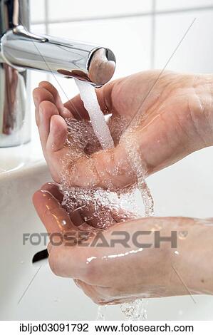 Stock Image - "Person washing their hands under running water from a faucet, symbolic image for water consumption". Fotosearch