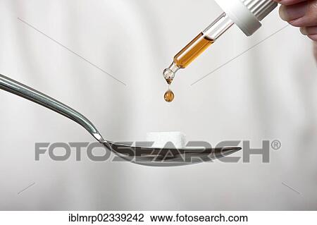 Stock Image - Pipette dripping medicine onto a sugar cube on a spoon. Fotosearch