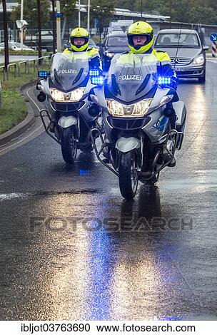 Stock Image - "Policemen wearing yellow helmets on motorcycles, police motorcycle patrol of the NRW Police riding with flashing blue lights during an emergency operation, Germany, Europe". Fotosearch