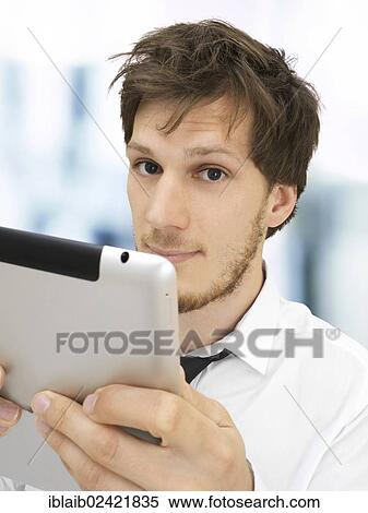 Portrait of a businessman holding an iPad, looking serious, concentrating View Large Photo Image Stock Photography - Portrait of a businessman holding an iPad, looking serious, concentrating. Fotosearch