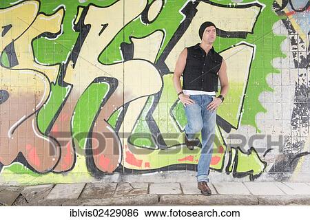 Stock Photograph - Portrait of a man standing in front of wall covered with graffiti. Fotosearch