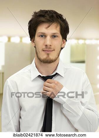 Portrait of a young man with a beard straightening his tie, friendly, relaxed View Large Photo Image Picture - Portrait of a young man with a beard straightening his tie, friendly, relaxed. Fotosearch