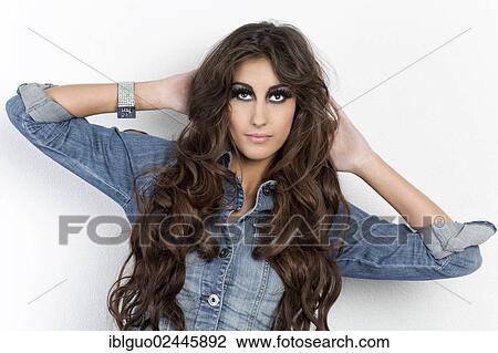 Stock Image - Portrait of a young woman with long hair wearing a denim jacket. Fotosearch