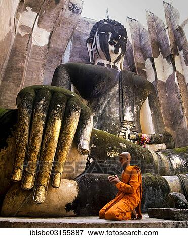 Stock Photo - "Praying monk neeling in front of the hand of the Buddha statue Phra Achana which is decorated with gold leaf, Wat Si Chum, Sukhothai Historical Park, Sukhothai, Sukhothai Province, Northern Thailand, Thailand, Asia". Fotosearch