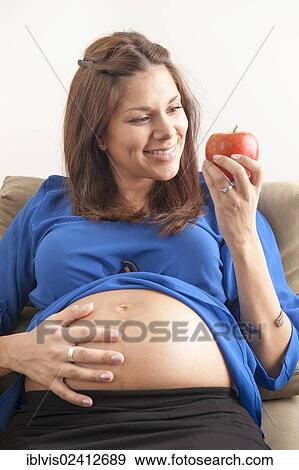 Pregnant woman holding hand on her stomach and eating an apple View Large Photo Image Stock Photo - Pregnant woman holding hand on her stomach and eating an apple. Fotosearch